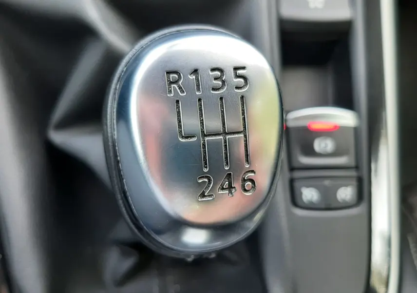 Gros plan sur le levier de vitesses manuel chromé du Renault Scénic IV gris Cassiopée, avec commandes électroniques en arrière-plan.