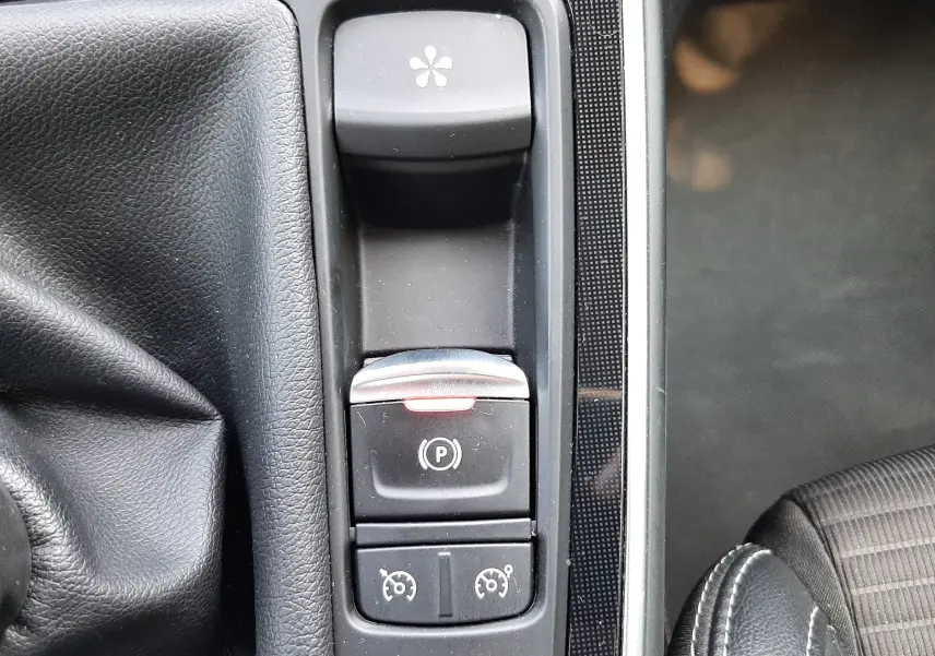Gros plan sur la console centrale du Renault Scénic IV gris cassiopée, montrant les commandes de frein à main électrique et régulateur de vitesse.