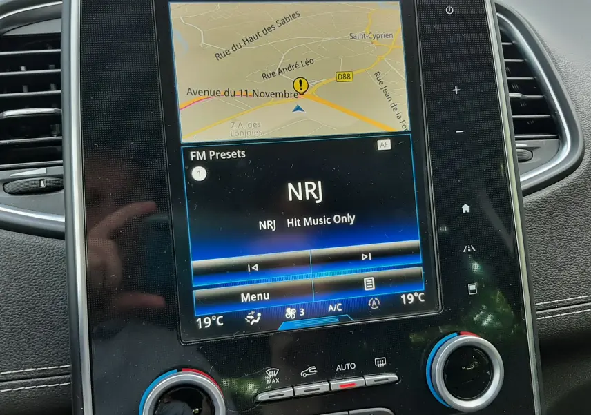 Vue rapprochée de l’écran tactile central du Renault Scénic IV gris cassiopée, affichant la navigation et la radio NRJ.