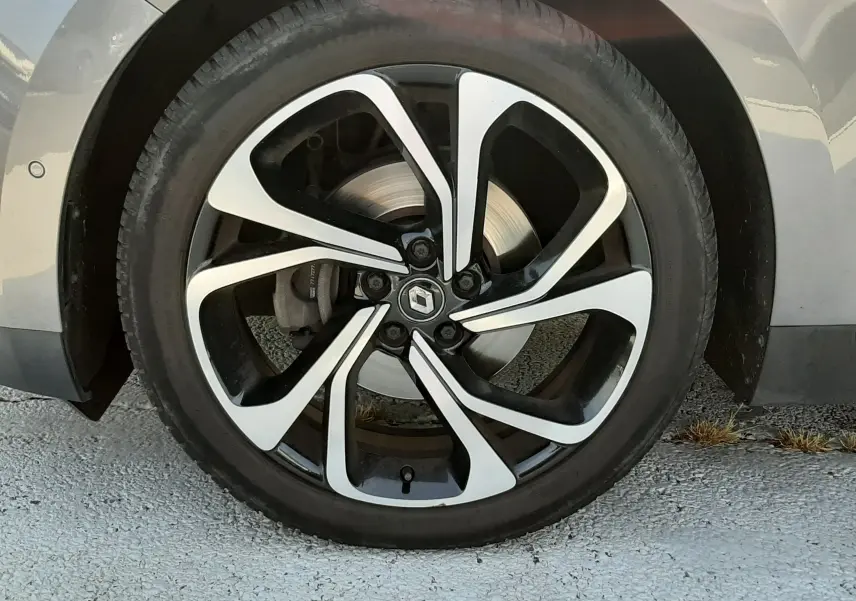 Gros plan sur la roue avant gauche du Renault Scénic IV gris Cassiopée, jante alliage noir et argentée au design moderne.