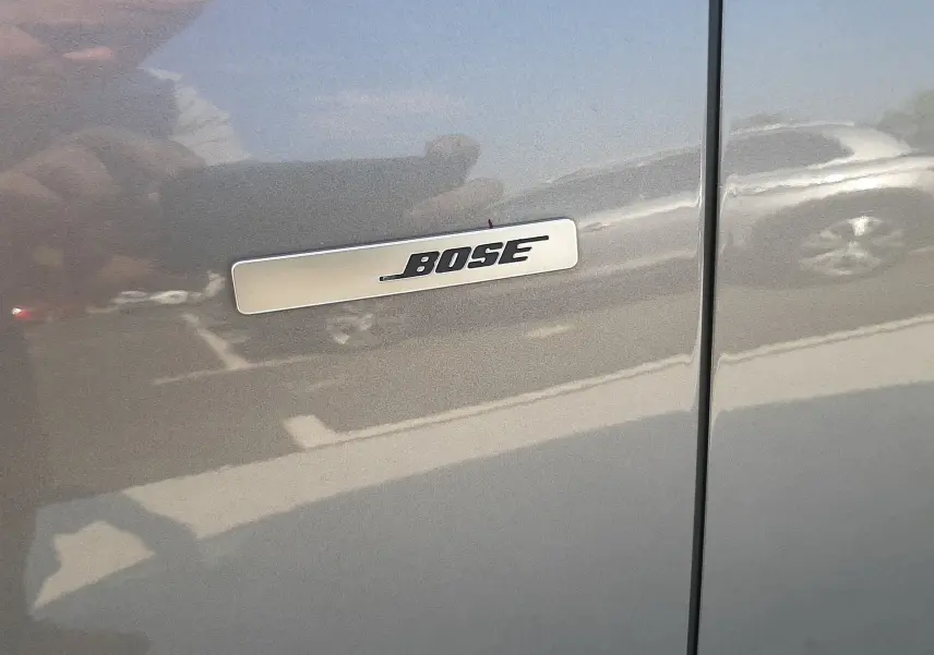Gros plan sur l’inscription Bose sur la porte gris cassiopée d’un Renault Scenic IV 2018, reflet de voiture en arrière-plan.