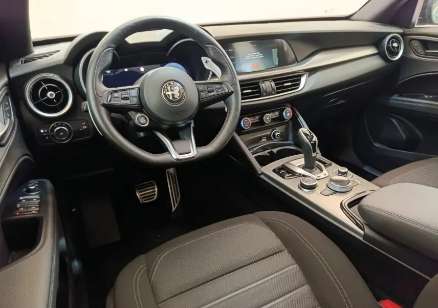 Intérieur noir de l'Alfa Romeo Stelvio 2024, vue côté conducteur sur le volant, tableau de bord et console centrale.