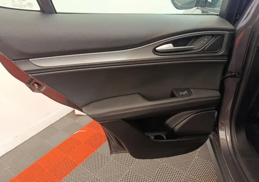 Porte côté gauche ouverte d'un Alfa Romeo Stelvio gris foncé, avec garniture noire et poignée alu intégrée.