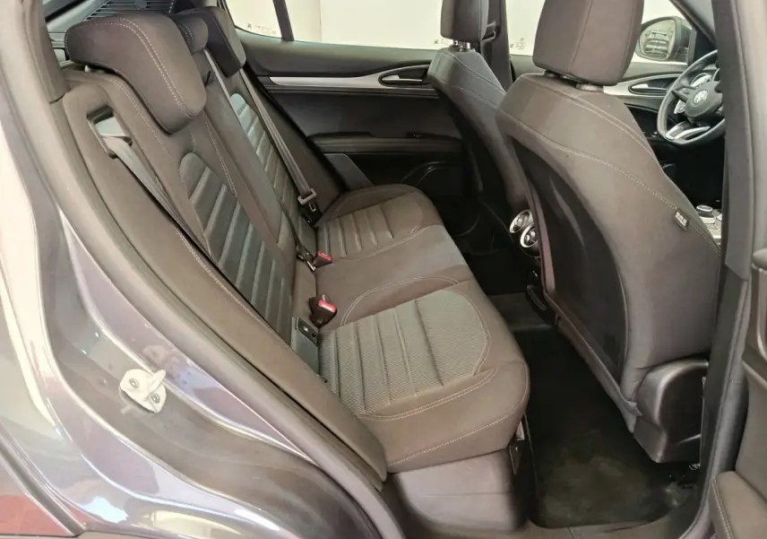 Vue côté gauche de l'habitacle arrière gris foncé de l'Alfa Romeo Stelvio 2024 avec sièges en tissu et aérateurs centraux.