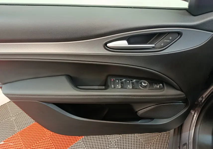 Gros plan sur la porte côté gauche de l'Alfa Romeo Stelvio gris foncé, avec commandes électriques et poignée argentée.
