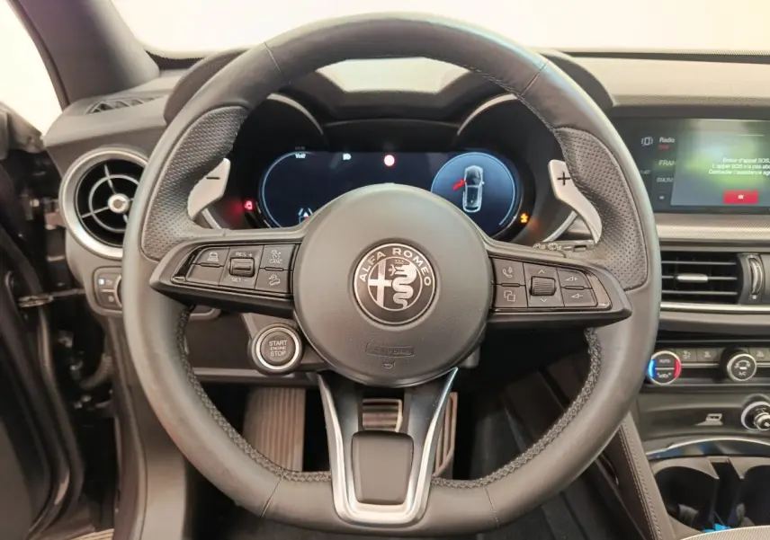 Vue rapprochée du volant cuir et aluminium de l'Alfa Romeo Stelvio 2024 avec tableau de bord numérique et commandes intégrées.