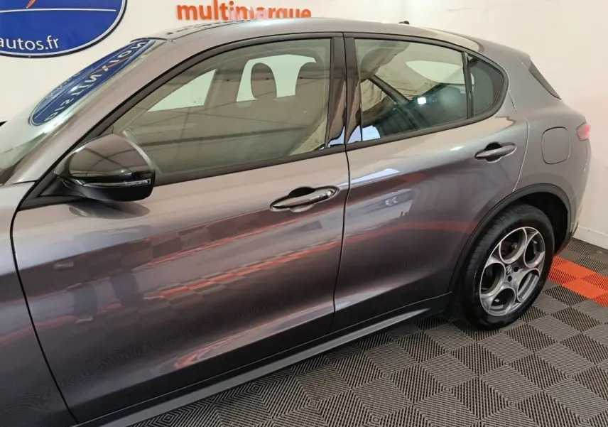 Profil côté gauche de l'Alfa Romeo Stelvio gris foncé 2024 avec jantes distinctives et rétroviseur noir brillant.