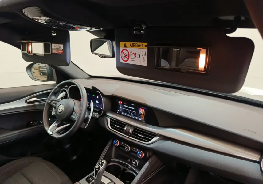 Intérieur de l'Alfa Romeo Stelvio 2024 vu côté conducteur, tableau de bord gris avec écran tactile et volant cuir.