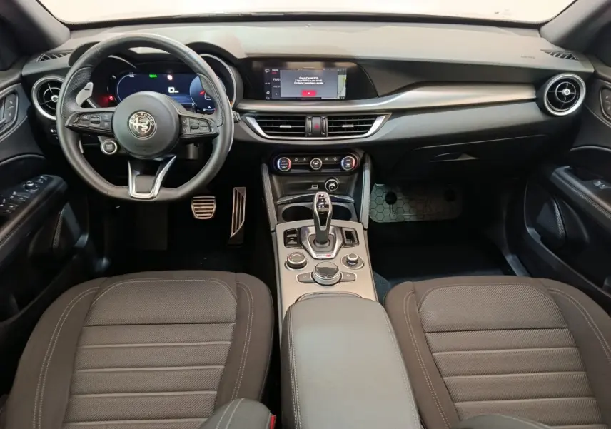 Vue intérieure avant de l'Alfa Romeo Stelvio Sprint 2024, tableau de bord noir avec écran tactile et volant cuir multifonctions.