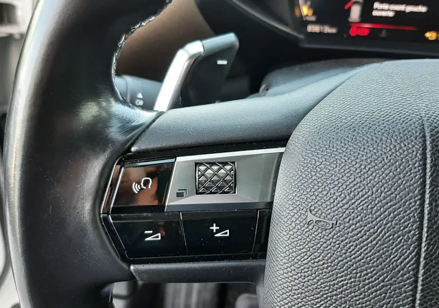 Gros plan sur les commandes du volant en cuir noir du DS3 Crossback 2019, avec affichage numérique en arrière-plan.