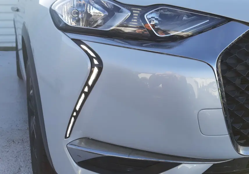 Gros plan sur l'avant gauche du DS3 Crossback blanc perle avec éclairage LED en forme de virgule et calandre noire.