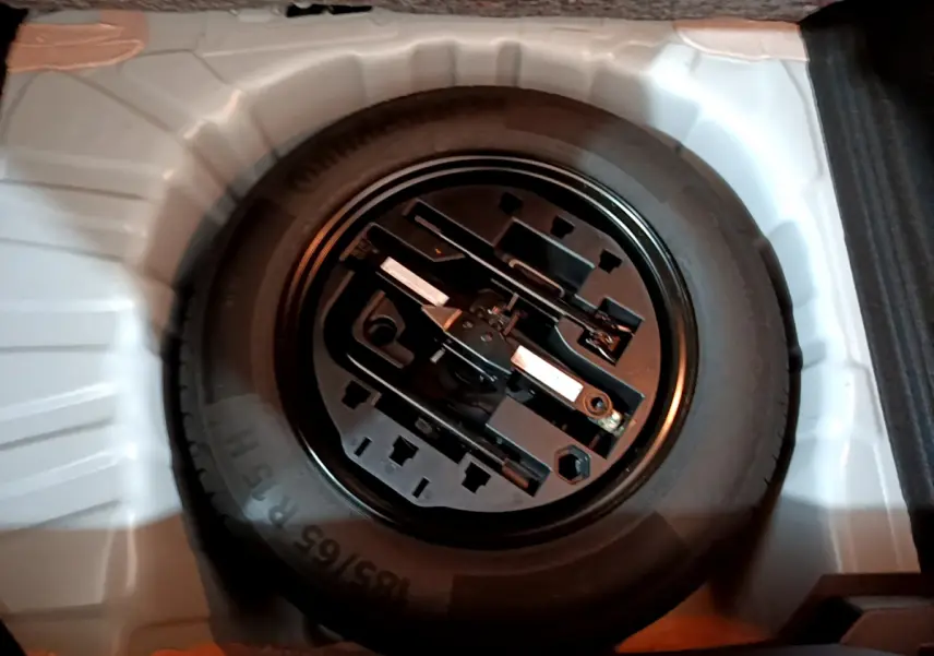 Roue de secours noire avec outils de changement dans le coffre blanc d'une Renault Clio Business TCe 90 2021.