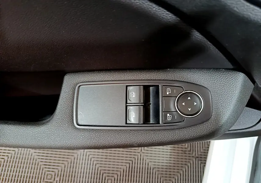 Gros plan sur les commandes de lève-vitres et réglage des rétroviseurs côté conducteur d'une Renault Clio blanche 2021.