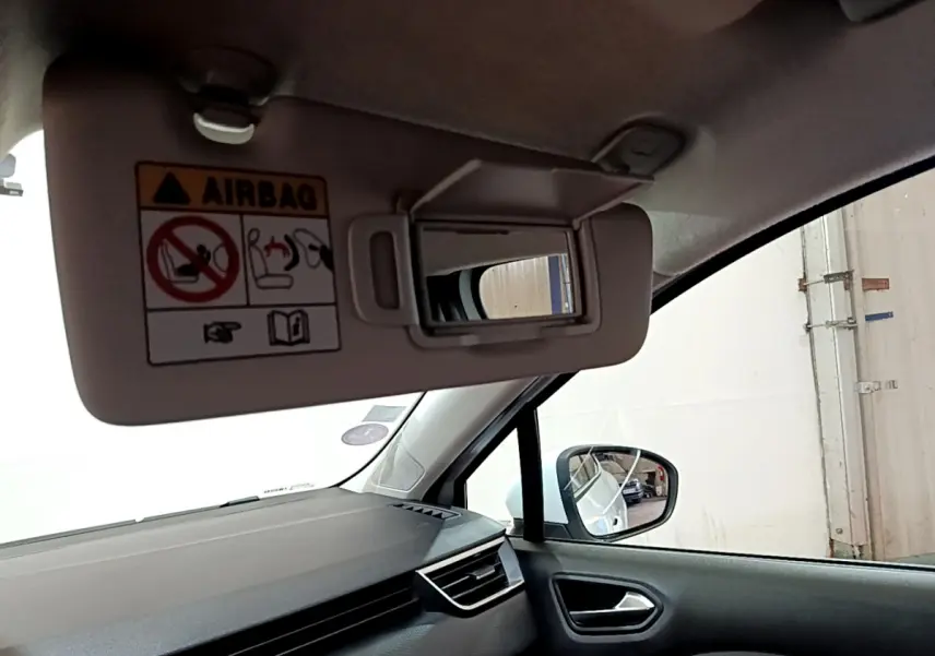 Détail de l'intérieur côté passager d'une Renault Clio blanche 2021, avec pare-soleil ouvert et miroir visible.