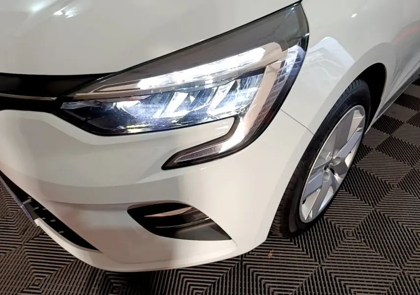 Gros plan sur le phare avant droit allumé d'une Renault Clio Business TCe 90 blanche, avec jante alu visible.