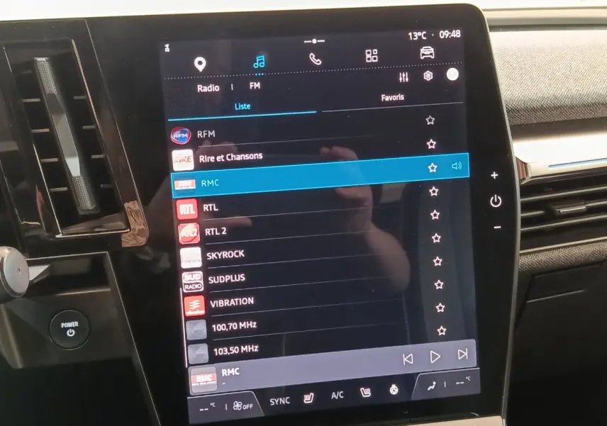 Vue rapprochée de l’écran tactile central de la Renault Mégane Techno EV60 bleu, affichant les stations radio FM.