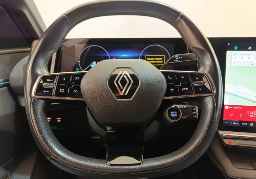 Vue rapprochée du volant cuir noir de la Renault Mégane électrique 2023 avec commandes multifonctions et écran tactile.