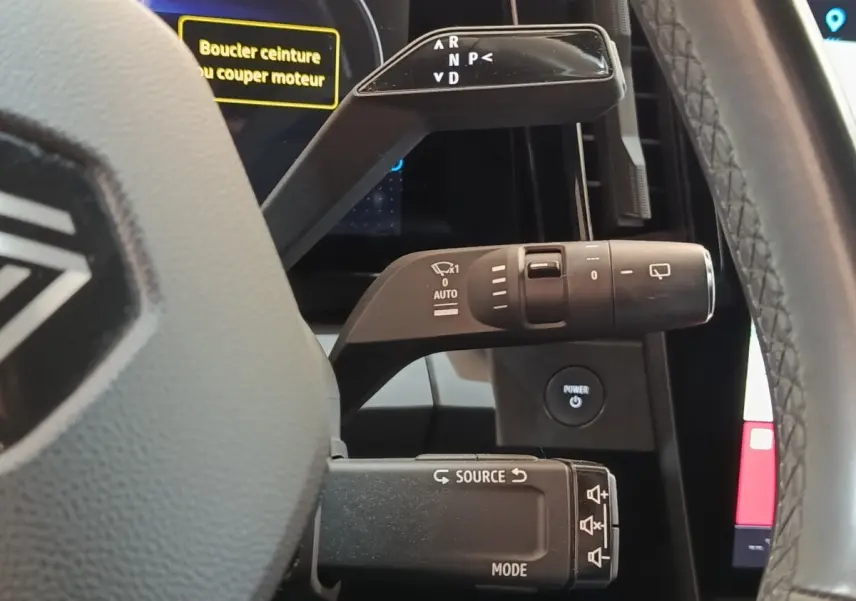Gros plan sur les commandes au volant d’une Renault Mégane électrique bleu, affichage digital et bouton Power visibles.