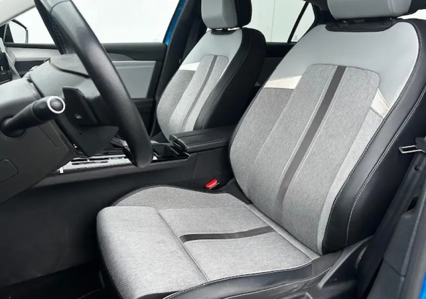Vue intérieure côté conducteur de l'Opel Astra bleu clair 2022, sièges tissu gris avec surpiqûres noires et volant cuir Premium.