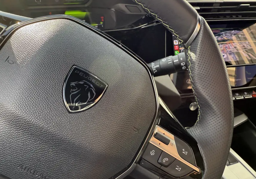 Gros plan sur le volant noir en cuir perforé du Peugeot 308 SW BlueHDi 130 EAT8 GT avec logo lion central.