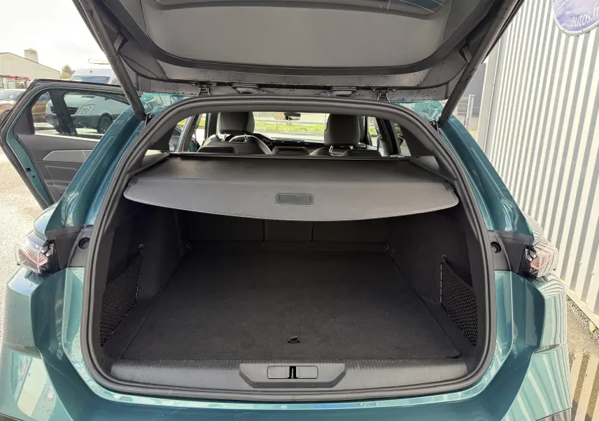 Coffre ouvert vu de l'arrière d'une Peugeot 308 SW Bleu Avartar, montrant l'espace de chargement avec cache-bagages déployé.