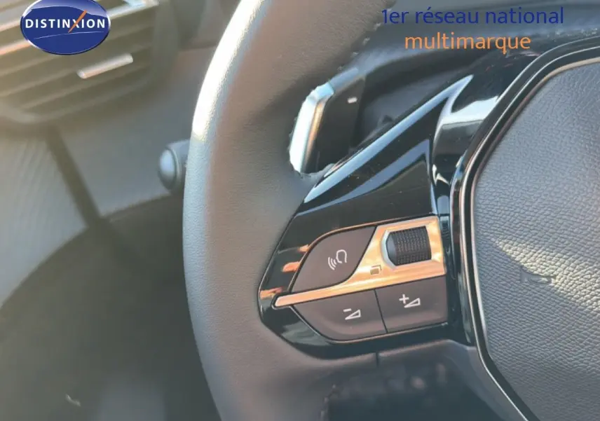 Détail des commandes sur le volant noir de la Peugeot 208 gris Artense Hybrid, mettant en valeur les boutons multifonctions.