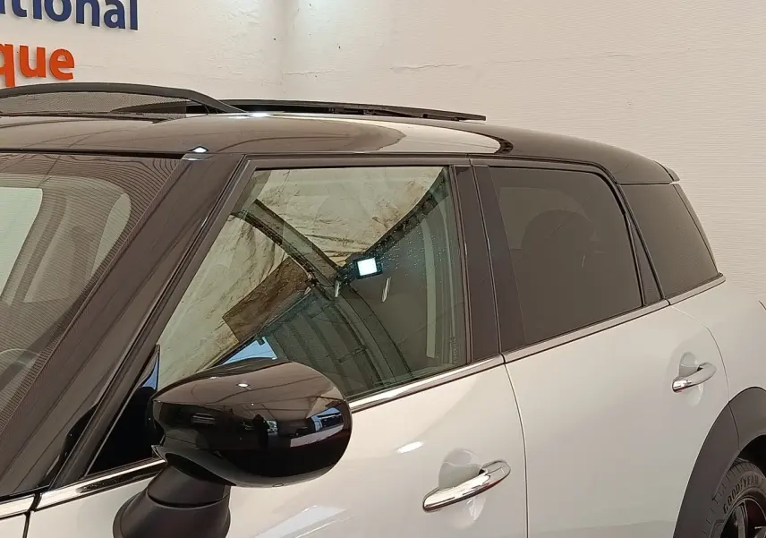 Vue latérale gauche d'une MINI Countryman hybride rechargeable blanche avec toit noir et rétroviseur noir brillant.