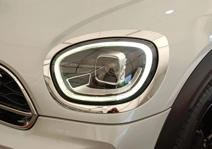 Gros plan sur le phare avant droit LED du MINI Countryman Cooper SE blanc, soulignant son design moderne et lumineux.