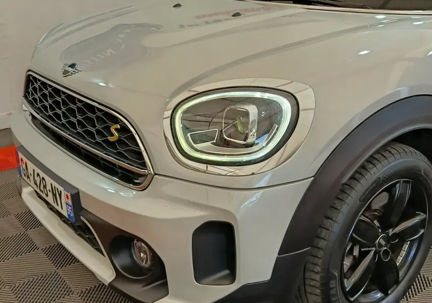 Vue 3/4 avant droit d'un MINI Countryman Cooper SE blanc avec phares LED et jantes noires brillantes.