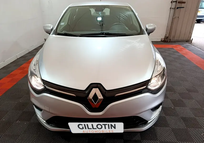 Vue avant d'une Renault Clio Business TCe 90 gris clair avec phares allumés dans un garage.