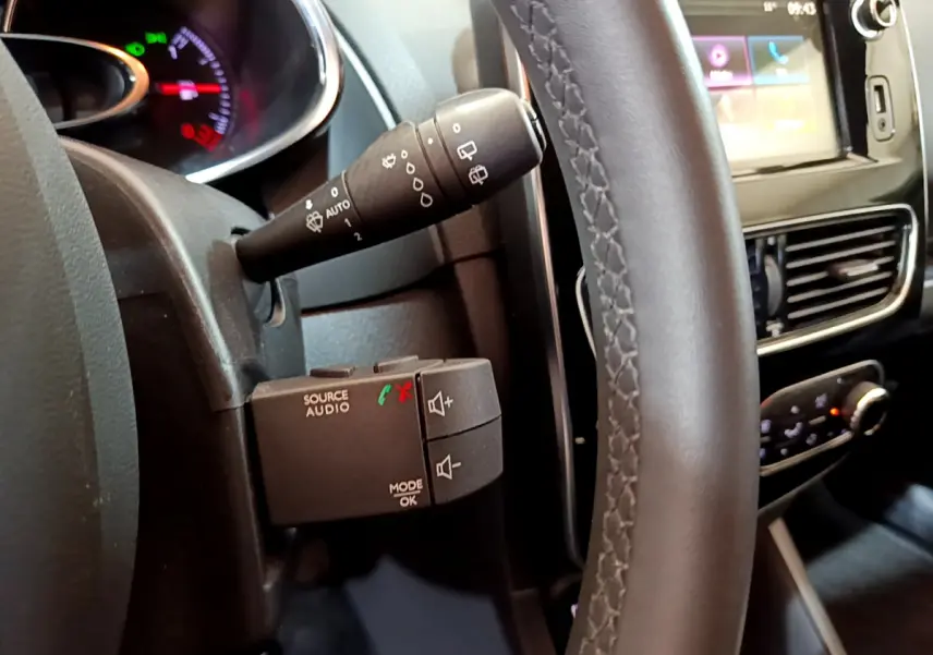 Vue rapprochée côté gauche du volant cuir de la Renault Clio Business gris clair, avec commandes audio et écran tactile visible.