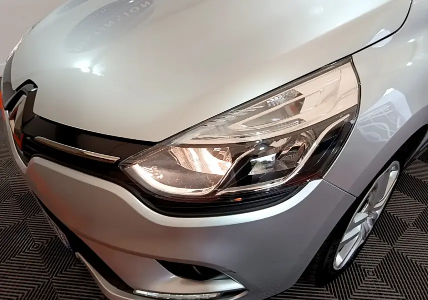 Gros plan sur l'avant droit gris clair de la Renault Clio 2019, mettant en valeur le phare et la calandre noire brillante.