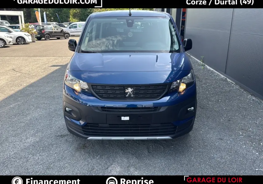 Vue avant d'un Peugeot Rifter bleu 2024 avec calandre noire et feux allumés sur un parking extérieur.