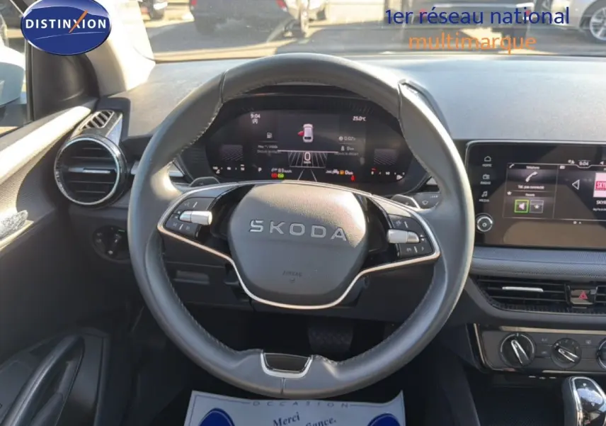 Vue intérieure centrée sur le volant SKODA noir et le tableau de bord digital lumineux d'une Fabia blanche Glacier 2025.