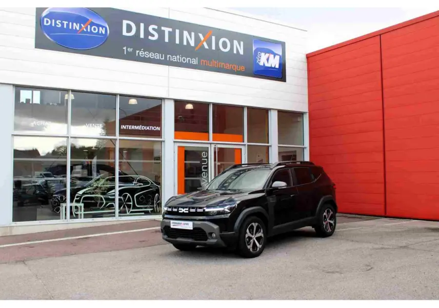 Dacia Duster III noir nacré vu en 3/4 avant droit devant un bâtiment commercial Distinxion.