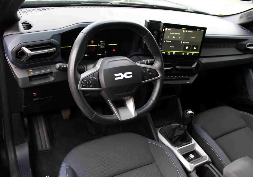 Intérieur du Dacia Duster III noir, vue du poste de conduite avec volant multifonction et écran tactile central.