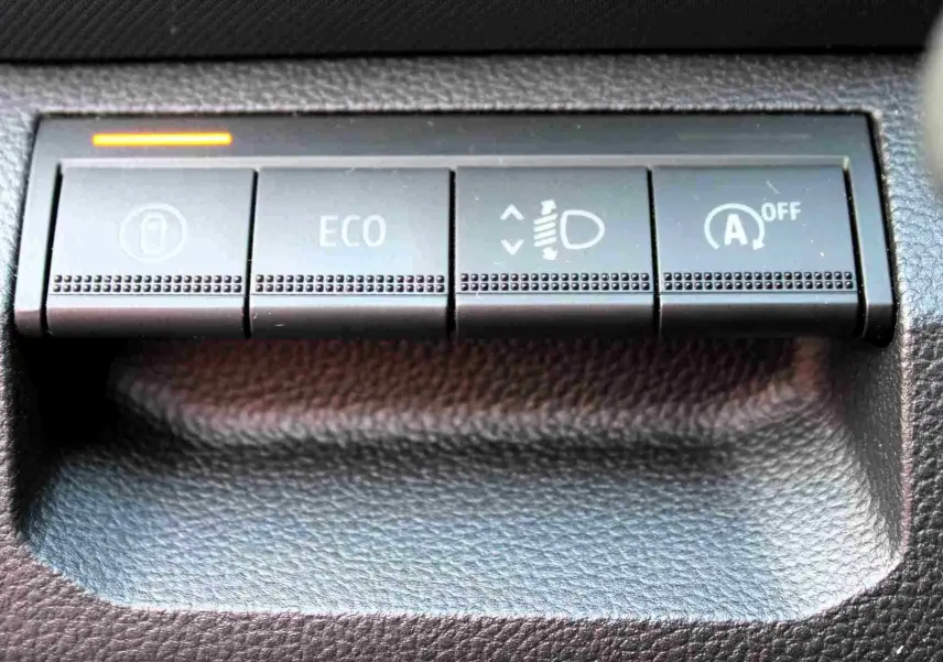 Gros plan sur les boutons de commande noirs du tableau de bord du Dacia Duster, avec témoin lumineux orange allumé.
