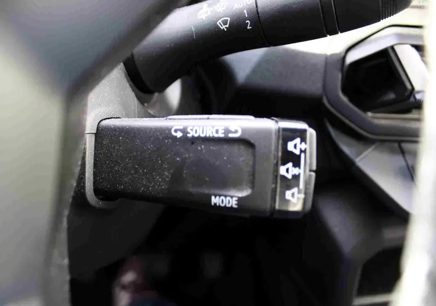 Gros plan sur la commande au volant noire du Dacia Duster 2025, avec inscriptions blanches "SOURCE" et "MODE".