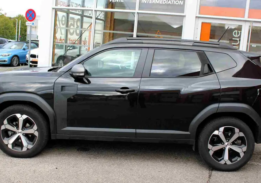 Vue de profil côté gauche d'un Dacia Duster noir nacré 2025 avec jantes alliage 18 pouces et barres de toit noires.