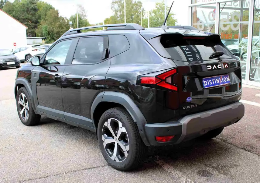 Vue 3/4 arrière droite du Dacia Duster noir nacré avec jantes alliage 18 pouces et barres de toit noires.
