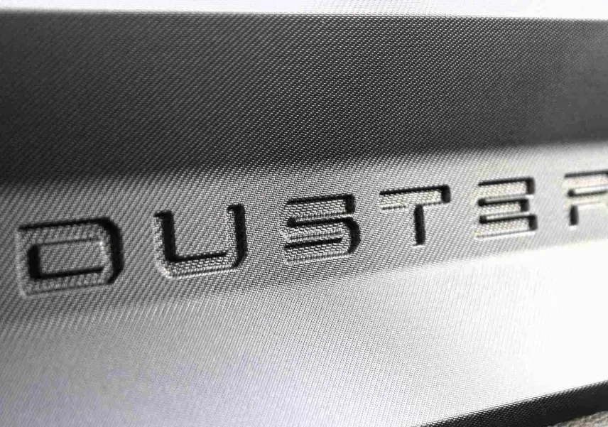 Gros plan sur le logo DUSTER en relief sur une surface intérieure grise du Dacia Duster noir.