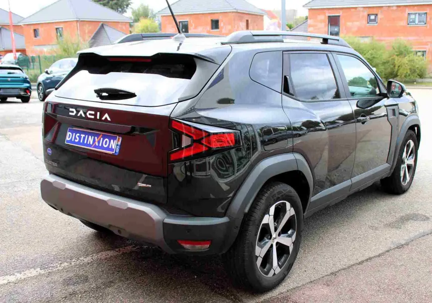 Vue 3/4 arrière droite du Dacia Duster 2025 noir nacré avec jantes alliage 18 pouces et barres de toit noires.