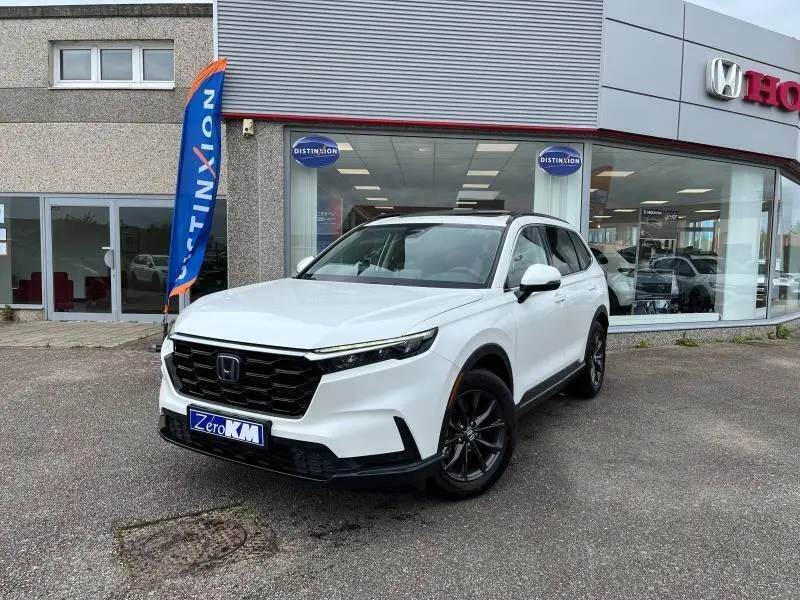 Honda CR-V 2024 blanc platine nacrée vu en 3/4 avant droit devant un showroom Honda avec jantes noires.