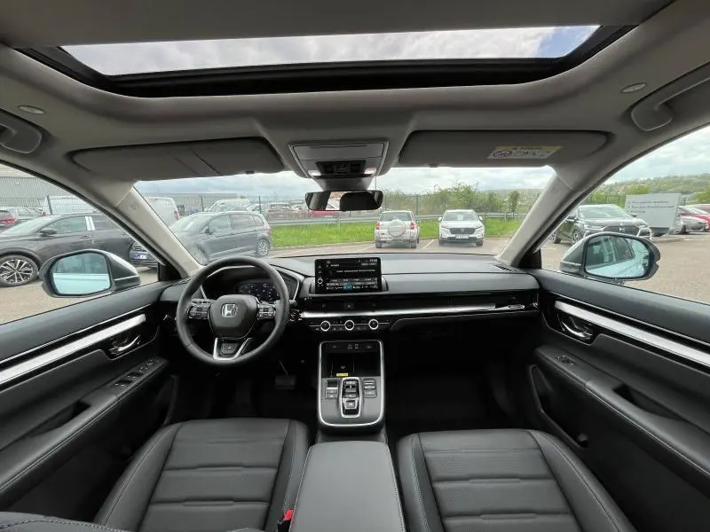 Vue intérieure avant du Honda CR-V 2024 blanc platine nacré, avec tableau de bord moderne et toit panoramique en verre.