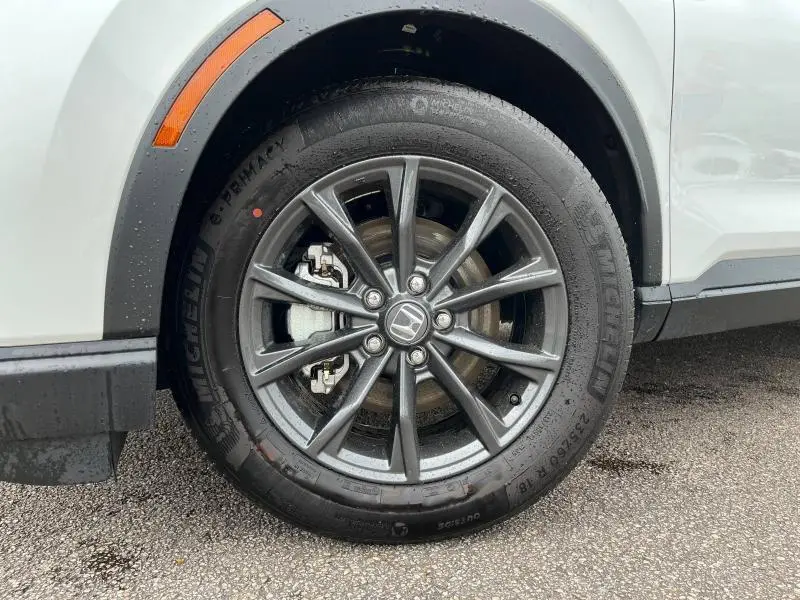 Gros plan sur la roue avant droite du Honda CR-V blanc platine nacré, jante alliage gris foncé avec logo Honda au centre.