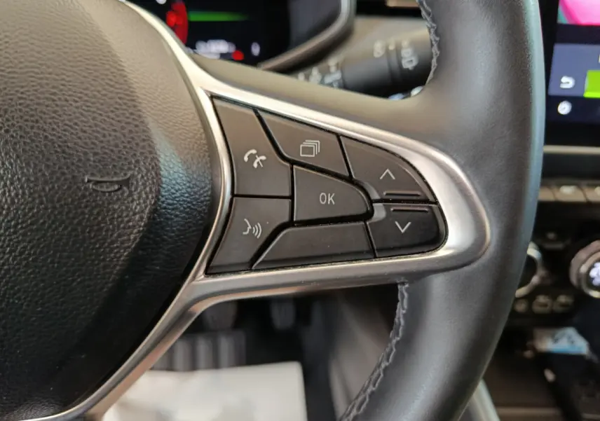 Gros plan sur les commandes du volant cuir noir de la Renault Clio Techno TCe 90, avec écran tactile en arrière-plan.