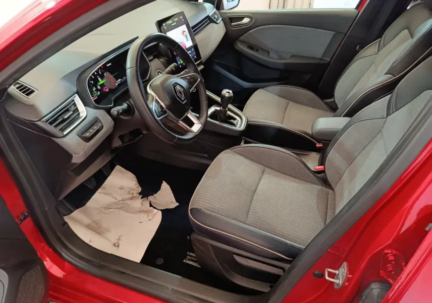 Vue intérieure côté conducteur de la Renault Clio Techno TCe 90 rouge 2024, avec tableau de bord numérique et sièges tissu gris.