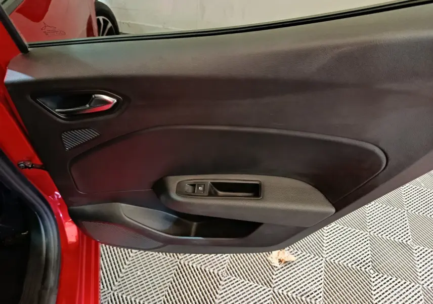 Vue rapprochée de la porte intérieure côté gauche rouge de la Renault Clio Techno TCe 90 avec poignée et commande de fenêtre.