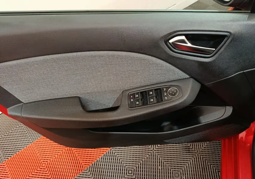 Vue rapprochée de la porte côté gauche rouge de la Renault Clio 2024 avec commandes électriques des vitres et poignée intérieure noire.