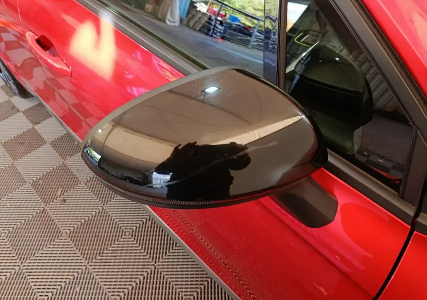 Rétroviseur noir côté gauche en gros plan sur Renault Clio rouge 2024, avec poignée de porte visible.